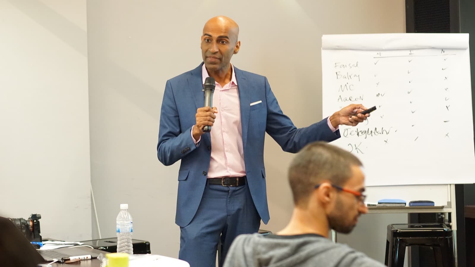 Indhran Seghar with a microphone leading a workshop beside a flip chart